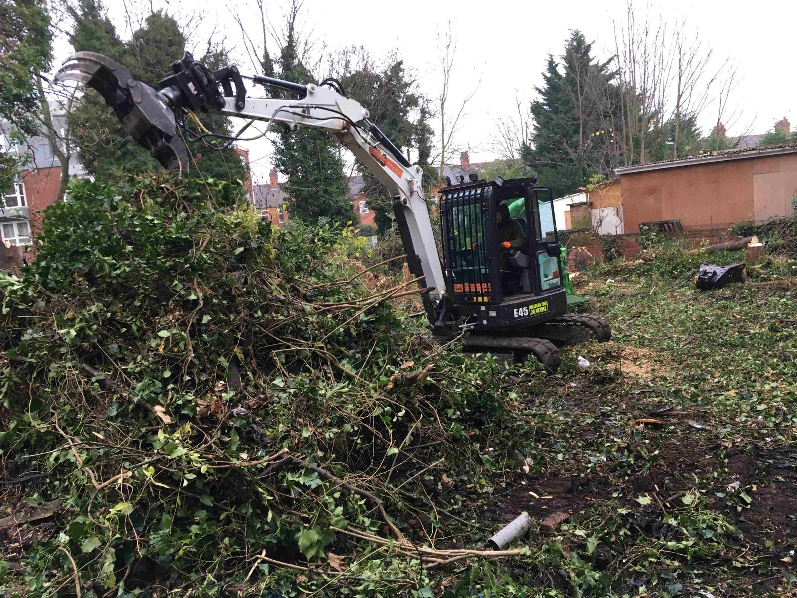 Mini excavator with grapple clearing a large pile of vegetation